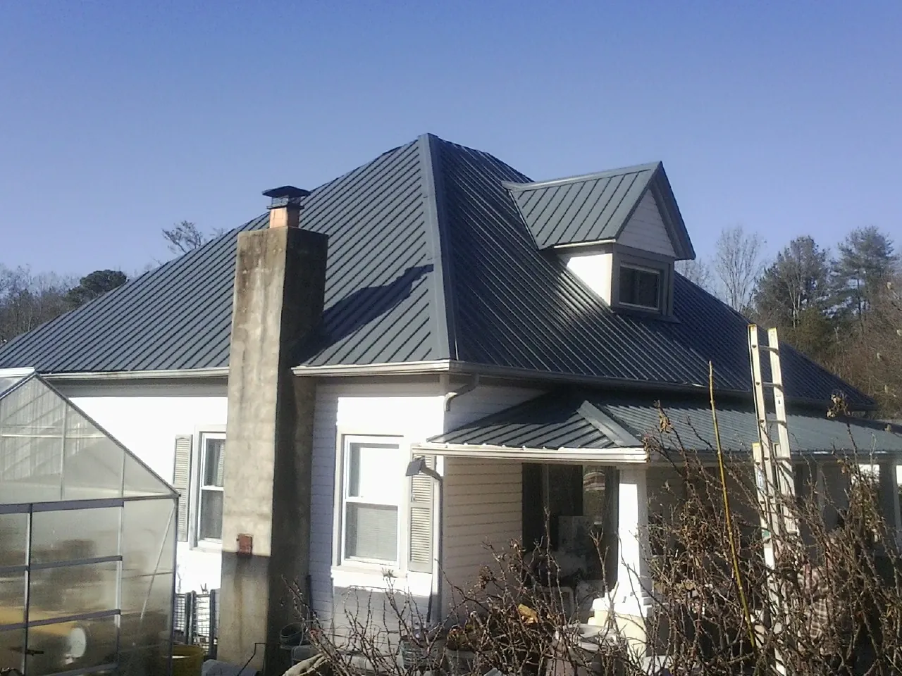 Dark blue standing seam metal roof on a white farmhouse with dormer — Slate & Tile Roof Repair by Roofing Brothers in East Petersburg