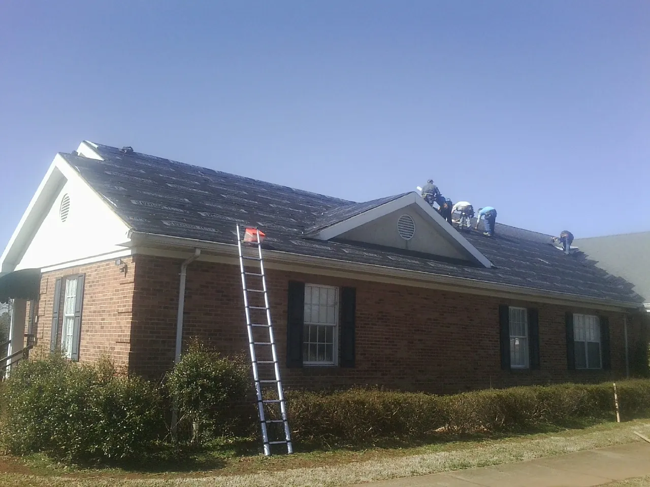 Crew tearing shingles off a brick ranch roof with a ladder set — Emergency Roof Repair work by our crew in East Petersburg