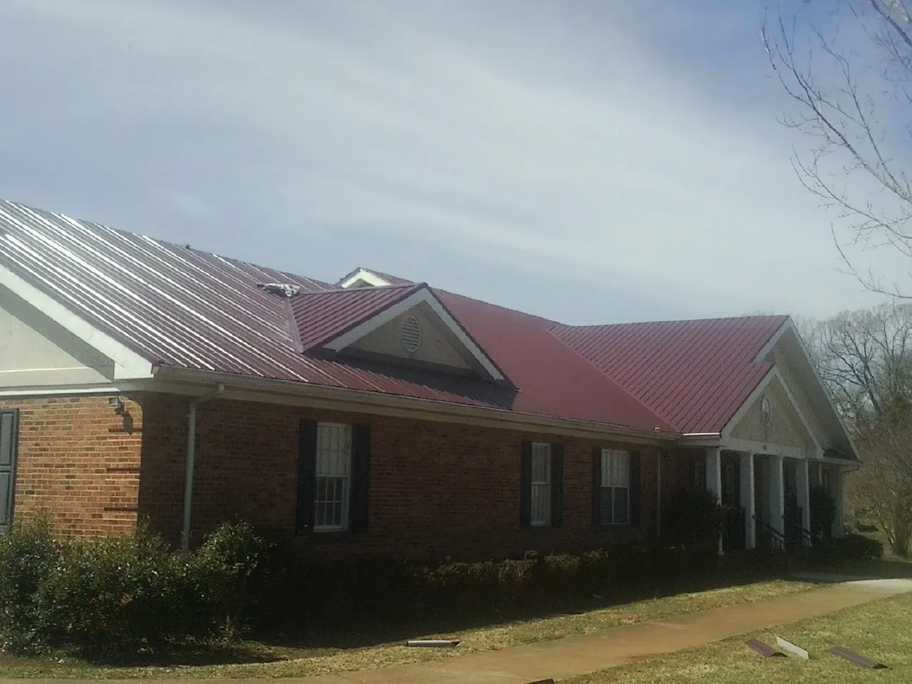 Red metal roof with gabled entries on a long brick building, from a Hail Damage Roof Repair job in East Petersburg