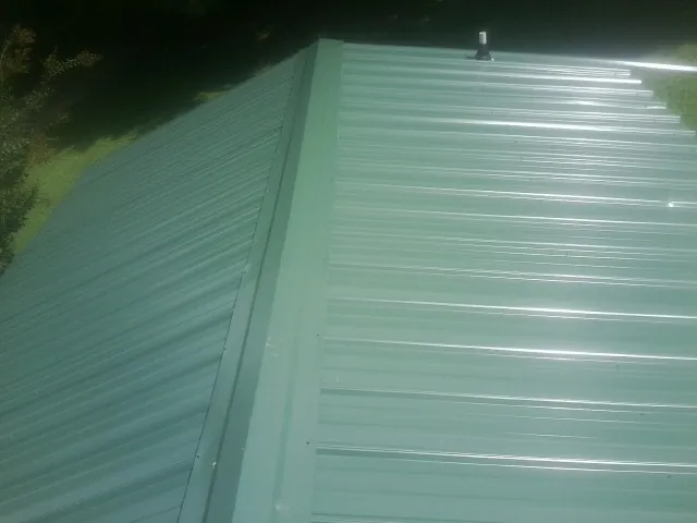 New green metal panels meeting at the ridge of a roof — Flat Roof Repair work by our crew in East Petersburg