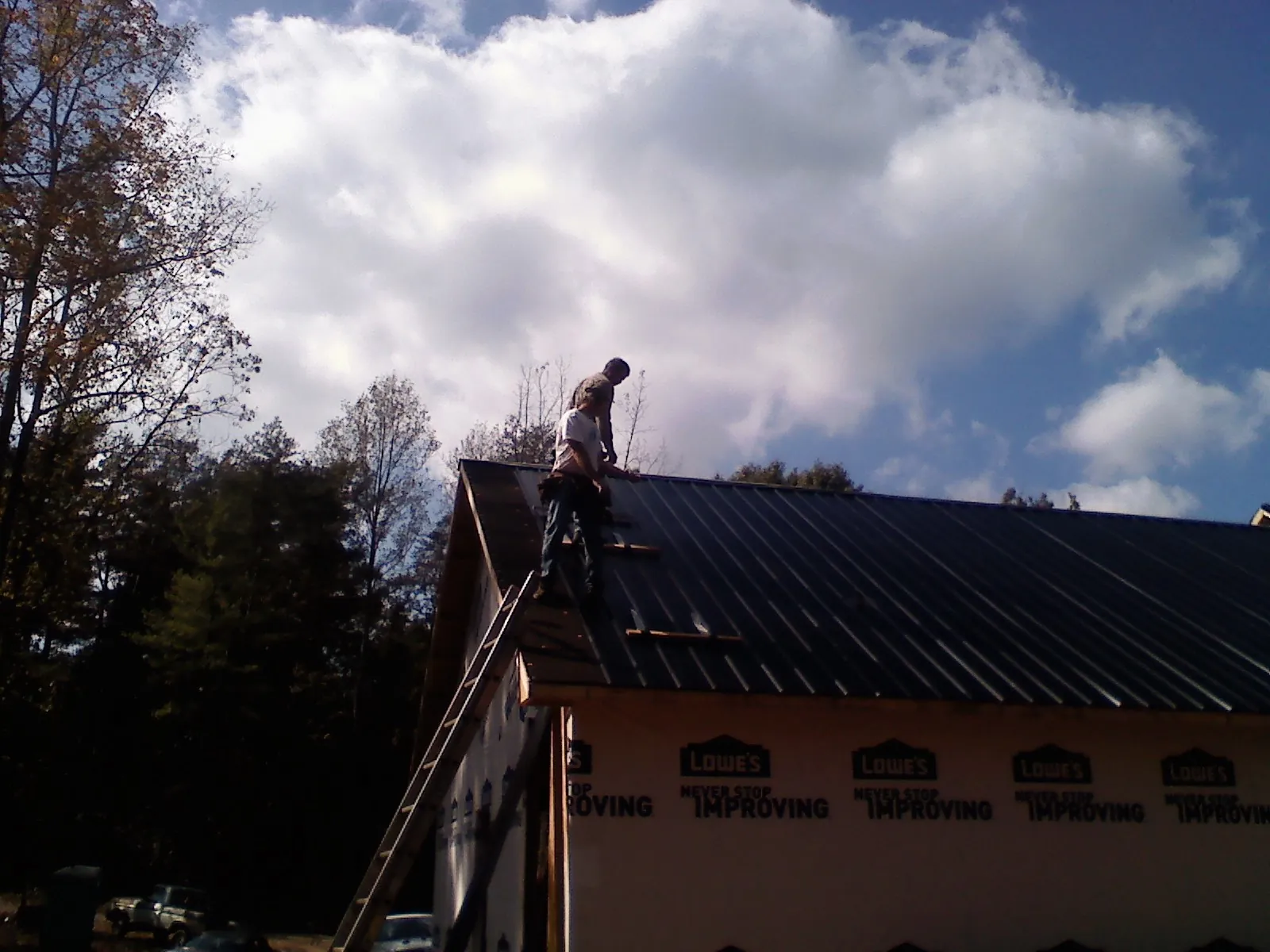 Roofer fastening dark metal panels high against a cloudy sky, from a Roof Inspection job in East Petersburg