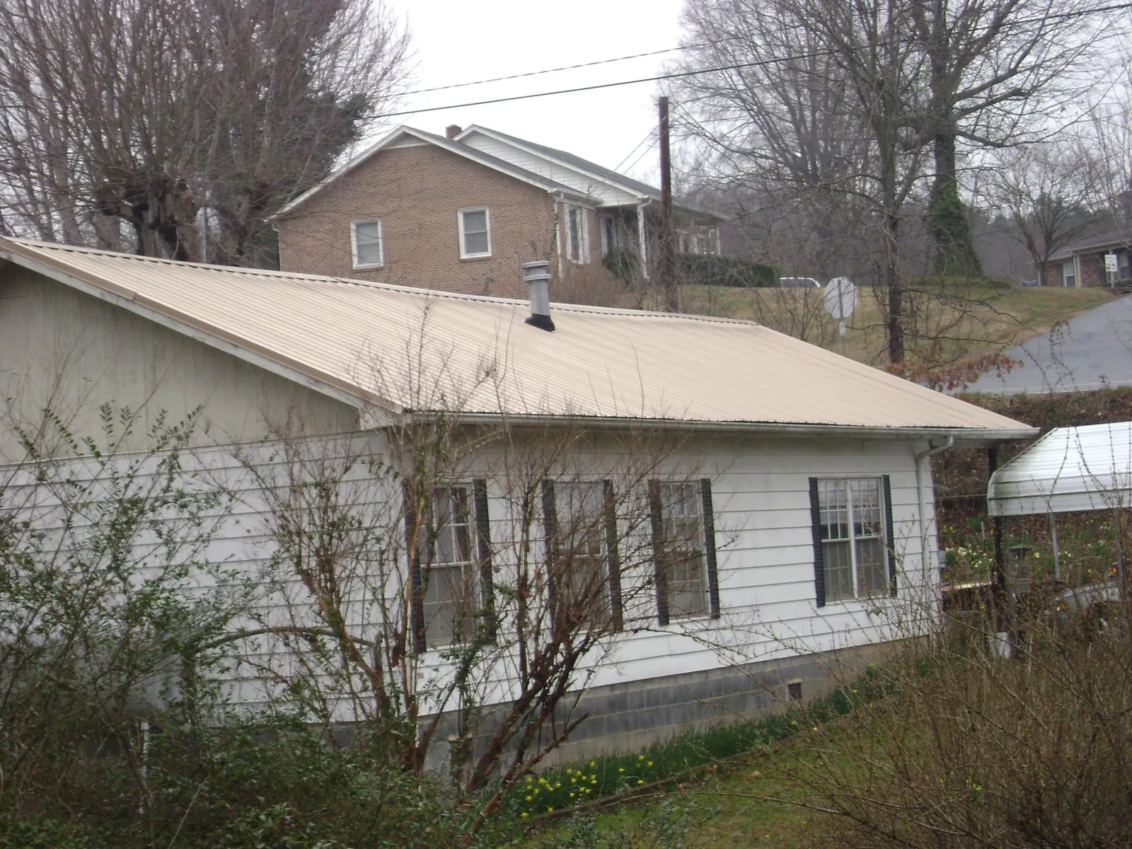 Tan metal roof on a white sided house set into a hillside — Commercial Roofing by Roofing Brothers in East Petersburg